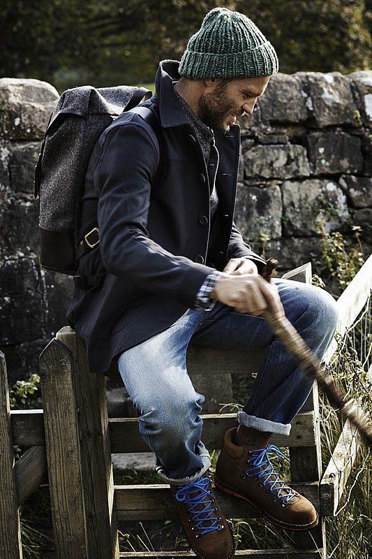 Person in green beanie, dark jacket, jeans outdoors with backpack.