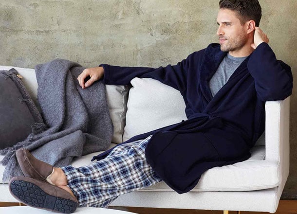 Man lounges in navy robe, plaid pants, and brown slippers.