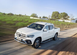 White Mercedes X-Class speeds on rural road.