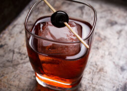 Red cocktail with cherry garnish on ice.