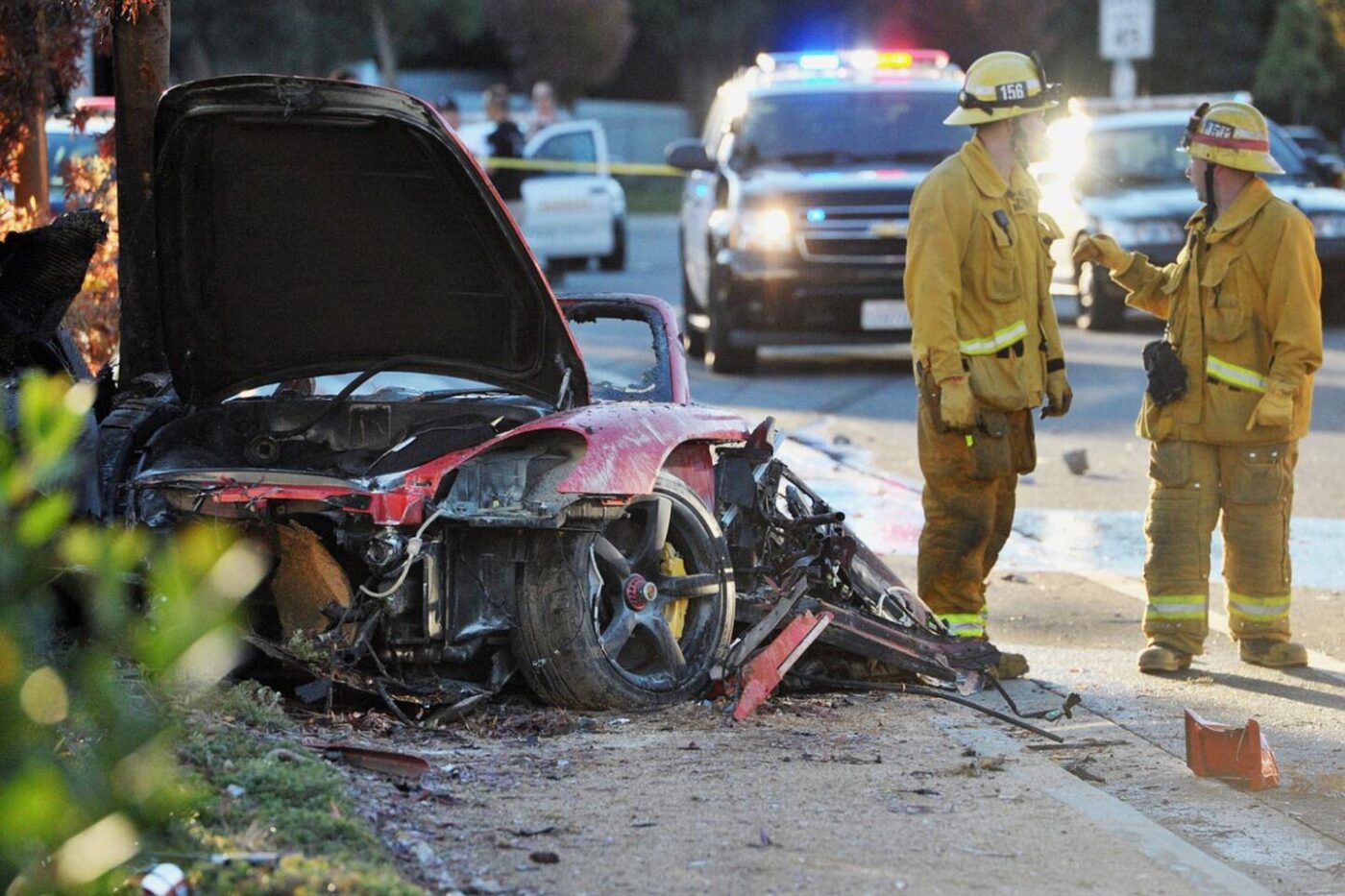 A red Porsche is wrecked; firefighters and police nearby.