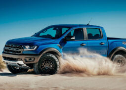 A blue Ford Raptor drives through the desert.