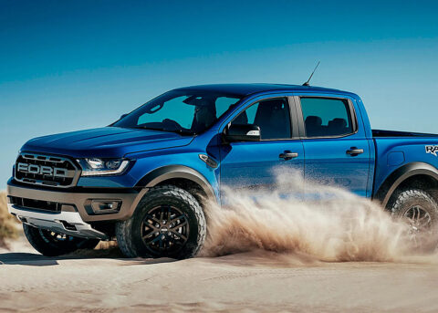 A blue Ford Raptor drives through the desert.