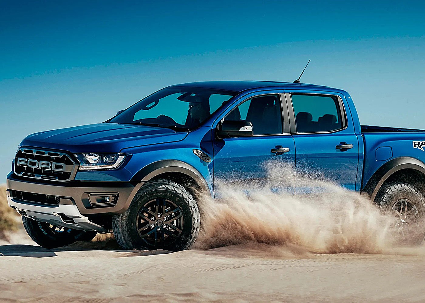 A blue Ford Raptor drives through the desert.