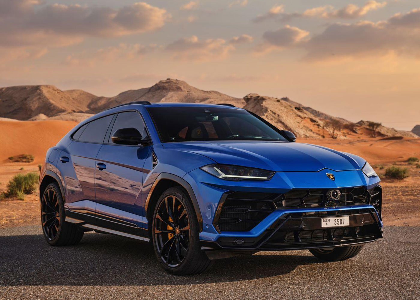 Blue Lamborghini Urus on desert road at sunset.