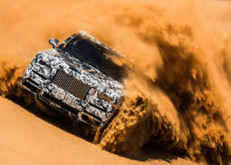 Rolls Royce Cullinan speeds through desert sand.
