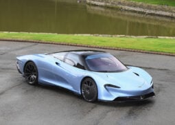 Blue McLaren hypercar parked near water.