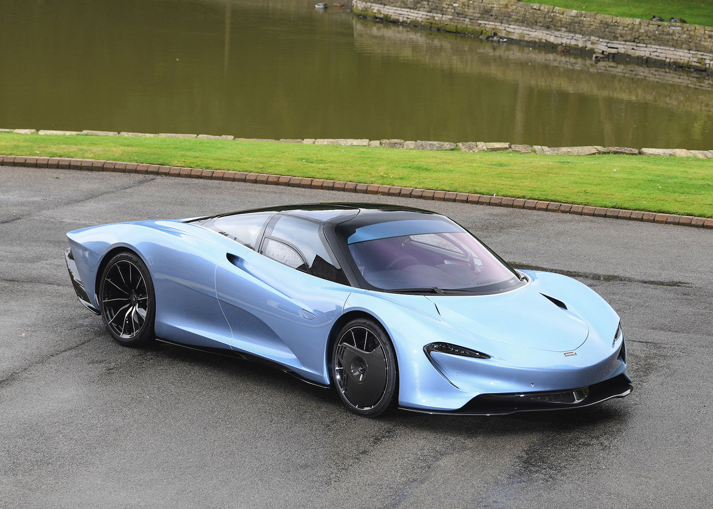 Blue McLaren hypercar parked near water.