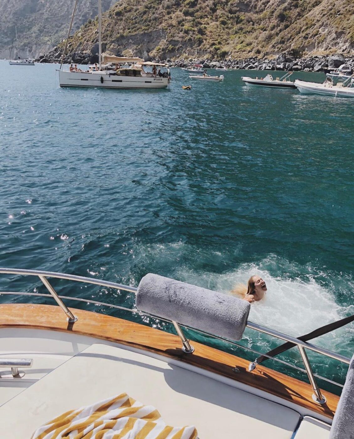 Swimmer glides by boat near rocky shoreline.