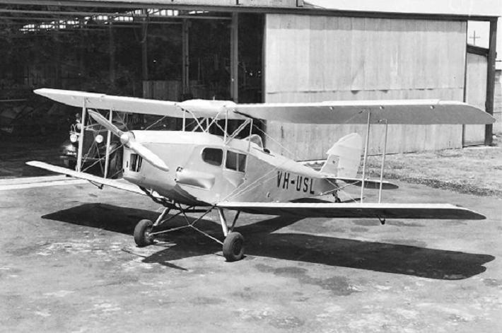 Vintage VH-USL biplane parked near hangar.