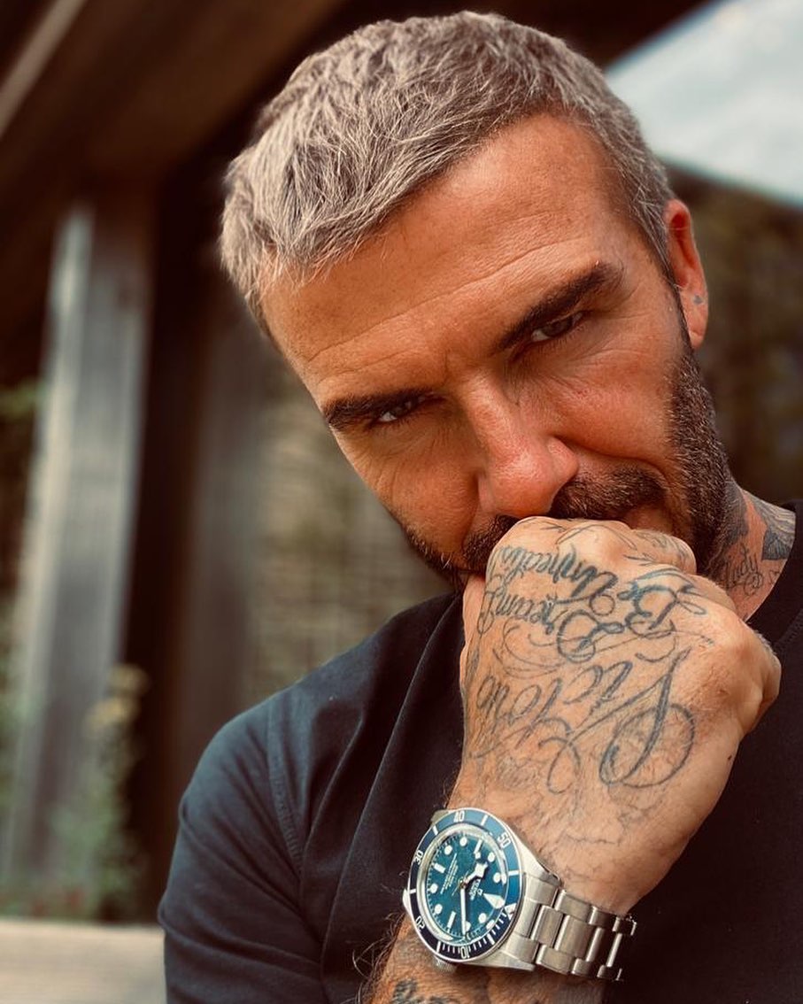 Tattooed man displaying Tudor watch, Beckham style.