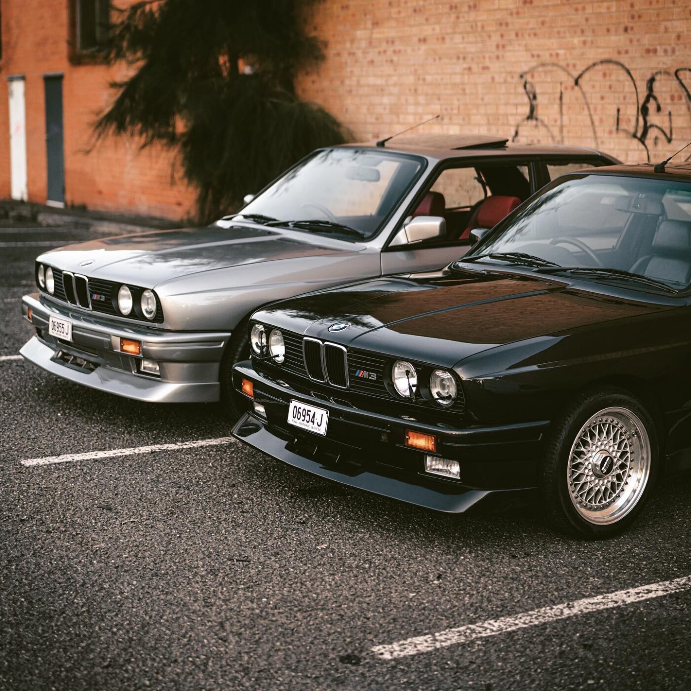 Two vintage BMWs parked by graffiti wall.