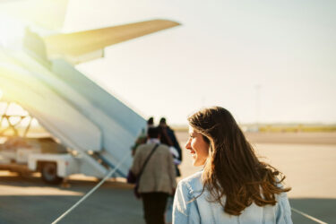 Woman boards Qantas plane under sunny sky.