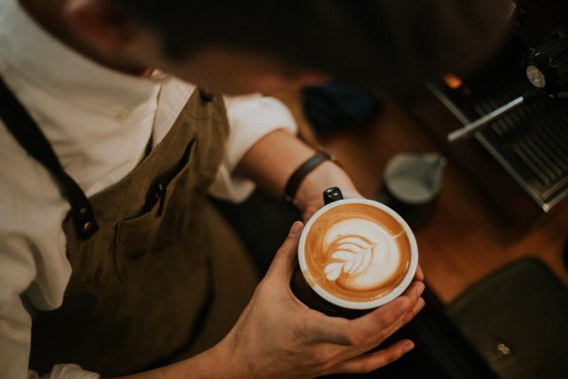 Barista with latte art prepares coffee orders.
