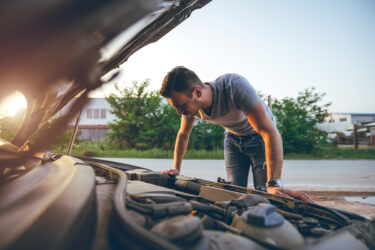 Man inspects car engine outdoors in Australia.