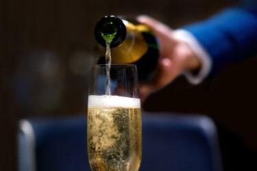 Person in blue jacket pours champagne flute.