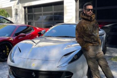 Man leans on silver Ferrari, red nearby.