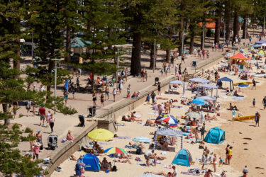 Busy Australian beach, sunbathers, boardwalk, umbrellas.