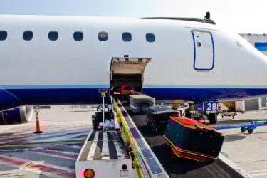 A handler loads luggage on sunny tarmac.