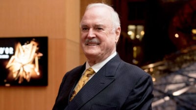 White-haired man in suit, John Cleese-style background.