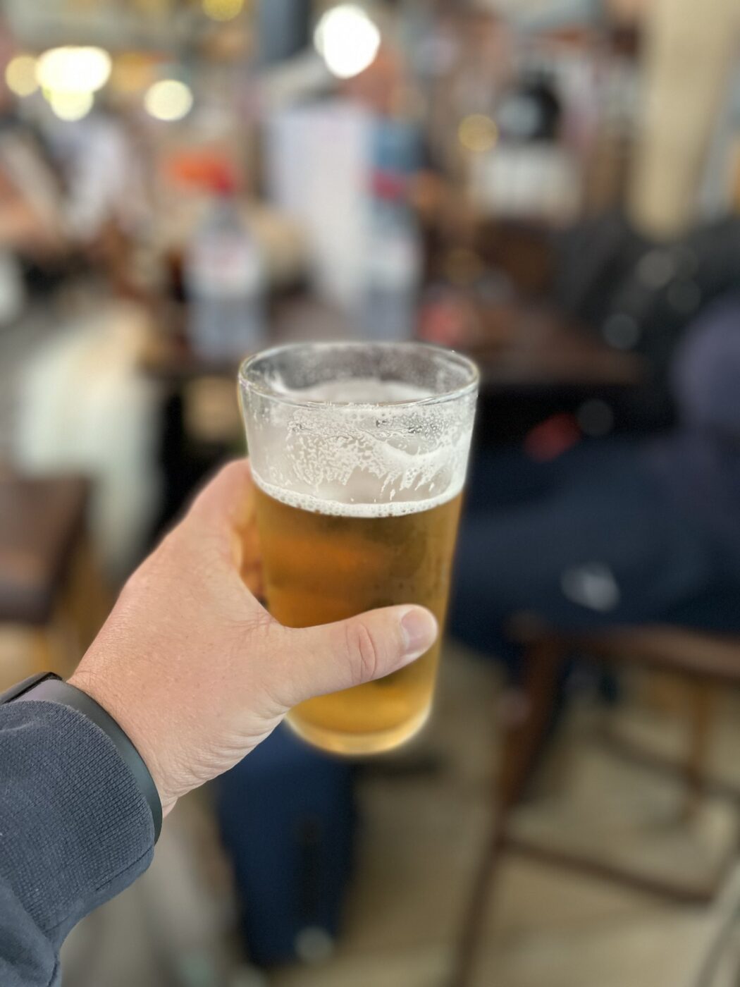 Hand holding beer pint at Australian airport lounge.