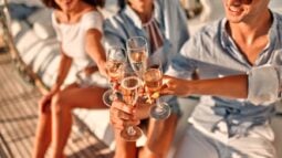 Three friends clink champagne glasses outdoors, celebrating.