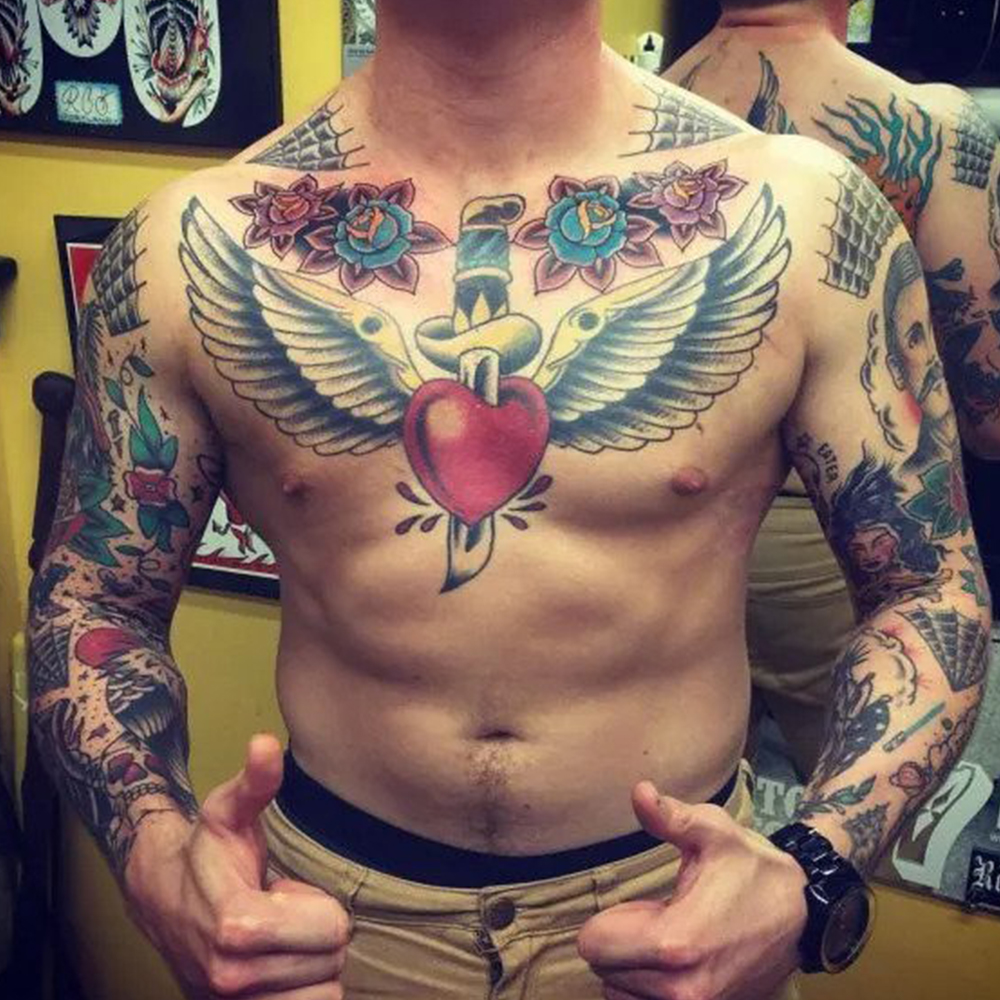 Real Heart With Wings And Banner Tattoo On Man Chest